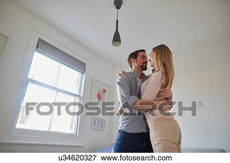 Mid adult couple hugging in living room View Large Photo Image Stock Photo - Mid adult couple hugging in living room. Fotosearch
