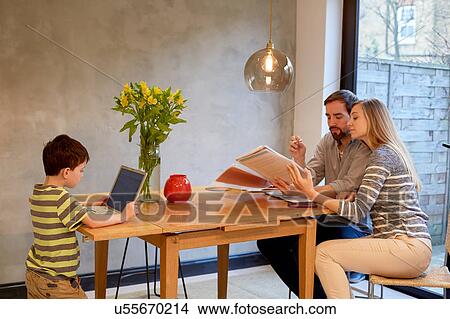 Mid adult couple looking at paperwork on dining table whilst son uses laptop View Large Photo Image Picture - Mid adult couple looking at paperwork on dining table whilst son uses laptop. Fotosearch