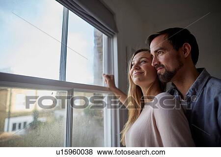 Stock Photo - Mid adult couple looking out through bedroom window. Fotosearch