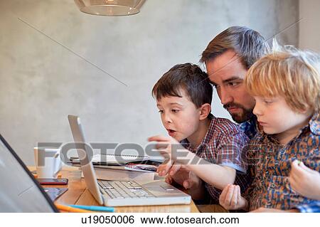 Mid adult man looking at laptop with two sons at dining table View Large Photo Image Stock Photograph - Mid adult man looking at laptop with two sons at dining table. Fotosearch