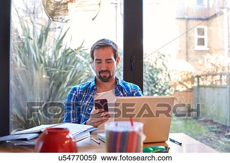 Mid adult man reading smartphone text at dining table View Large Photo Image Stock Photo - Mid adult man reading smartphone text at dining table. Fotosearch