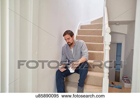 Stock Photography - Mid adult man sitting on staircase reading smartphone texts. Fotosearch