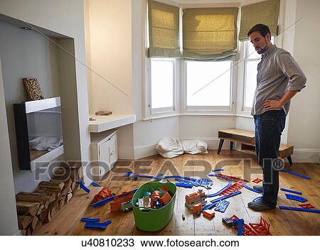 Stock Image - Mid adult man staring at toys scattered in living room. Fotosearch