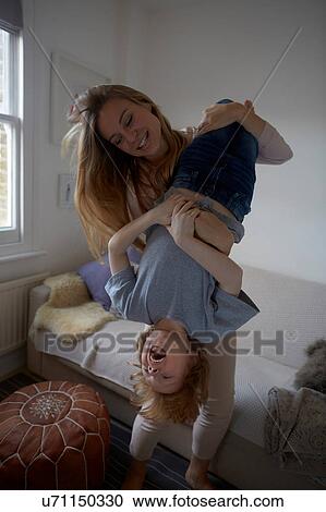 Stock Image - Mid adult woman holding son upside down in living room. Fotosearch