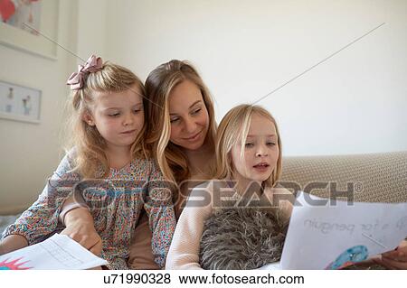 Stock Photo - Mid adult woman looking at drawings with daughters in living room. Fotosearch