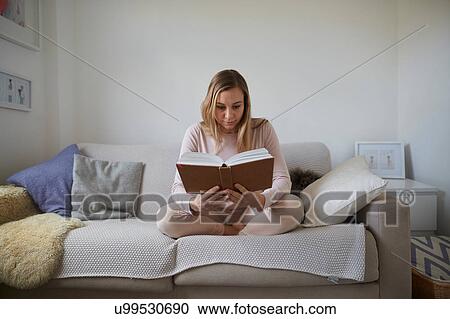 Mid adult woman reading book on living room sofa View Large Photo Image Stock Image - Mid adult woman reading book on living room sofa. Fotosearch
