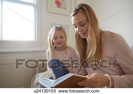Stock Image - Mid adult woman reading to daughter in living room. Fotosearch