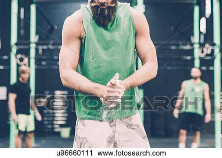 Stock Image - Mid section of male cross trainer chalking hands in gym. Fotosearch