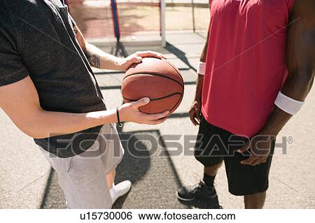 Stock Photograph - Mid section of two male basketball players with ball on basketball court. Fotosearch