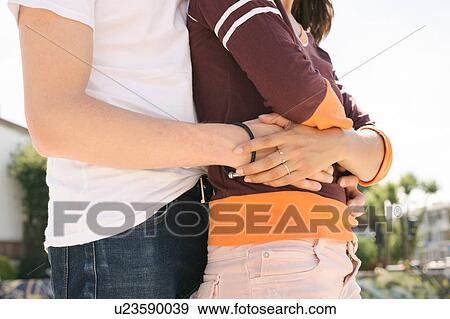 Stock Photo - Mid section of young man with arms around girlfriend in city skatepark. Fotosearch