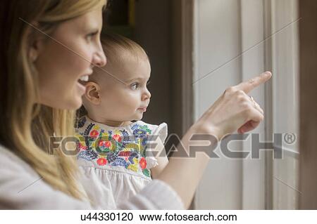 Stock Image - Mother and daughter (18-23 months) looking through window. Fotosearch