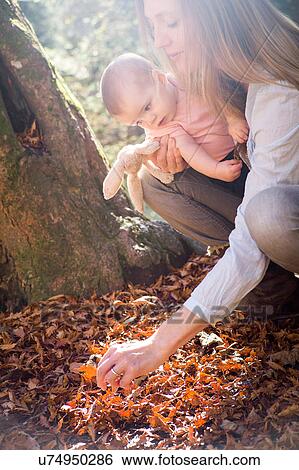 Stock Photograph - Mother and daughter crouching investigating leaves on forest floor. Fotosearch