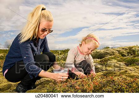 Stock Image - Mother and daughter outdoors, picking blueberries. Fotosearch