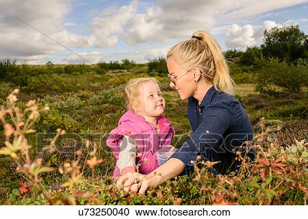 Stock Image - Mother and daughter outdoors, picking blueberries. Fotosearch