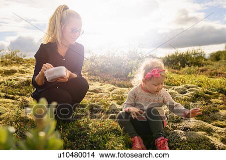Mother and daughter sitting in field, searching for blueberries View Large Photo Image Picture - Mother and daughter sitting in field, searching for blueberries. Fotosearch