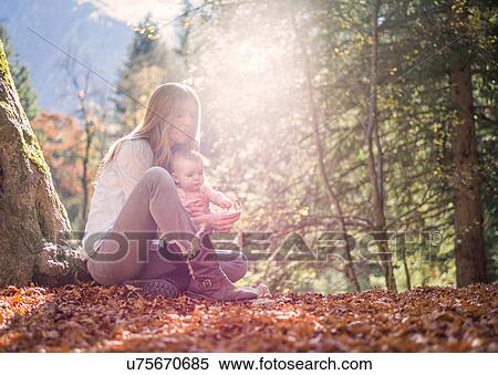 Stock Photography - Mother and daughter sitting on autumn leaf covered forest floor. Fotosearch