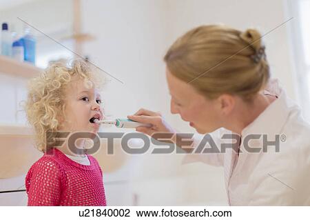 Stock Image - Mother helping daughter (4-5) brush teeth. Fotosearch