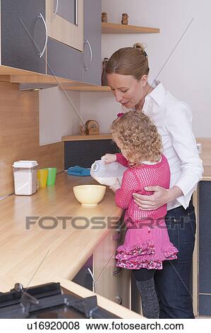 Stock Photo - Mother helping daughter (4-5) pour milk into bowl. Fotosearch
