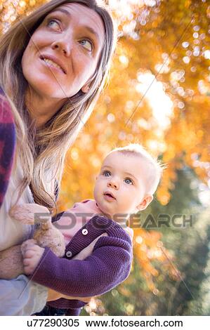 Stock Photography - Mother holding baby girl in forest looking away. Fotosearch