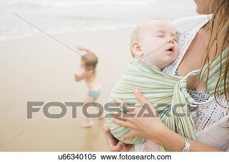 Stock Photography - Mother holding baby son (6-11 months), daughter (2-3) dancing on beach. Fotosearch