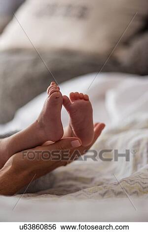 Stock Photograph - Mother holding son's (0-1 months) feet in bedroom. Fotosearch