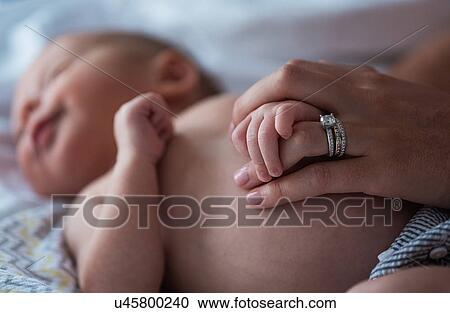 Stock Image - Mother holding son's (0-1 months) hand in bedroom. Fotosearch