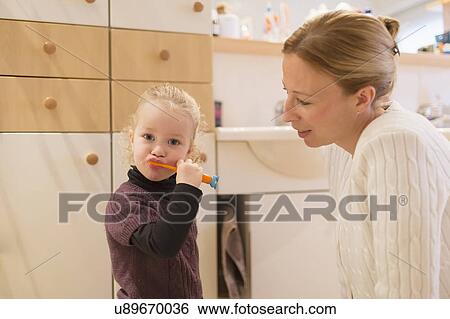 Stock Photograph - Mother looking at daughter (4-5) brushing teeth in bathroom. Fotosearch