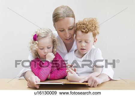 Stock Photo - Mother reading book to son (8-9) and daughter (4-5). Fotosearch