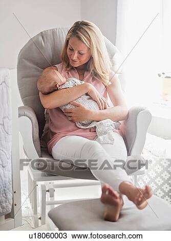 Stock Image - Mother sitting in armchair and holding baby son (0-1 months). Fotosearch