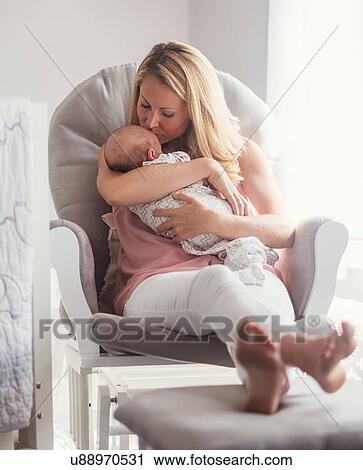 Stock Image - Mother sitting in armchair and kissing baby son (0-1 months). Fotosearch