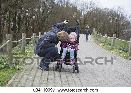 Mother talking to daughter (4-5) sitting in stroller, boy (8-9) walking in background View Large Photo Image Stock Photo - Mother talking to daughter (4-5) sitting in stroller, boy (8-9) walking in background. Fotosearch