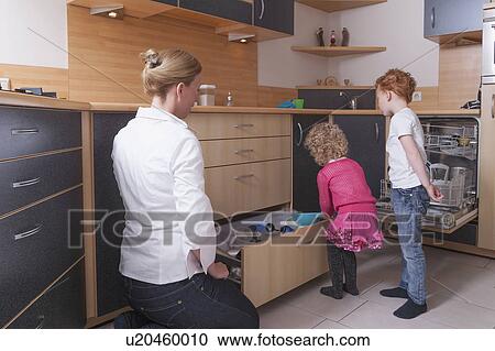 Stock Image - Mother watching daughter (4-5) and son (8-9) sorting cooking utensils. Fotosearch