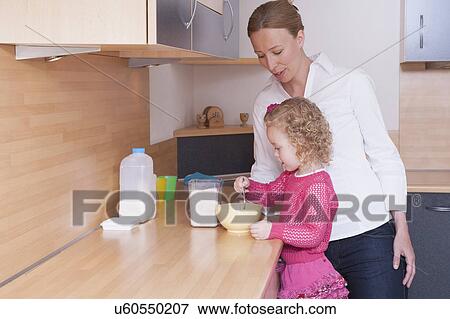 Stock Photo - Mother watching daughter (4-5) mixing ingredients in bowl. Fotosearch