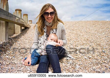 Mother with baby girl sitting on shingle beach looking at camera smiling View Large Photo Image Stock Photography - Mother with baby girl sitting on shingle beach looking at camera smiling. Fotosearch