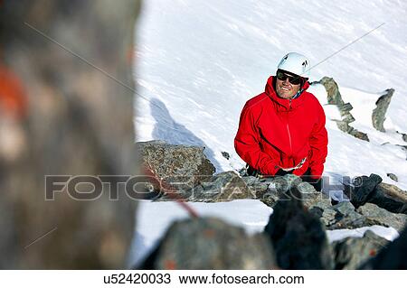 Stock Image - Mountaineer on snow covered mountain looking up smiling, Saas Fee, Switzerland. Fotosearch