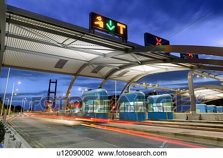 Stock Image - Night view of cars passing through toll booth at bridge. Fotosearch