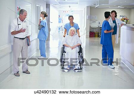 Stock Image - Nurse pushing senior female patient in wheelchair onto hospital ward. Fotosearch
