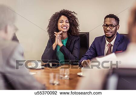 Stock Image - Over shoulder view of businessman and woman listening at boardroom meeting. Fotosearch