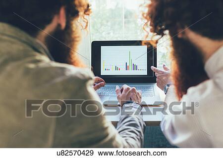Over shoulder view of male twins working on laptop in office View Large Photo Image Stock Photo - Over shoulder view of male twins working on laptop in office. Fotosearch