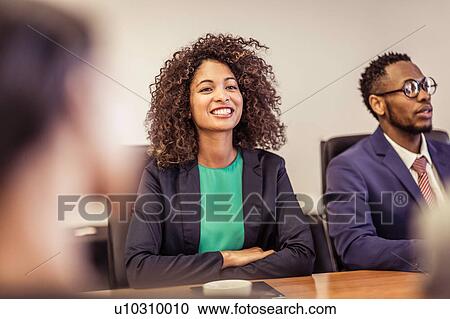 Stock Image - Over shoulder view of young businesswoman at boardroom meeting. Fotosearch