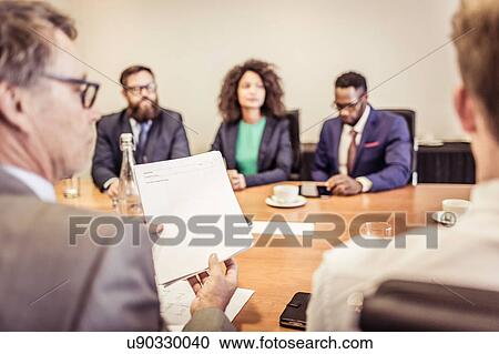 Stock Image - Over the shoulder view of businesswomen and men at conference table meeting. Fotosearch
