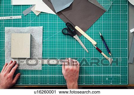 Stock Image - Overhead detail of hands, paper, cutting mat, ruler, scalpel and scissors in print studio. Fotosearch