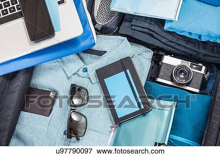 Stock Photo - Overhead detail of packed suitcase with blue shirt, retro camera, laptop, smartphone and notebook. Fotosearch