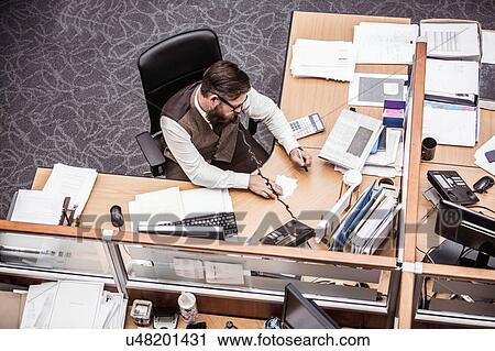 Stock Image - Overhead view of businessman talking on landline at office desk. Fotosearch