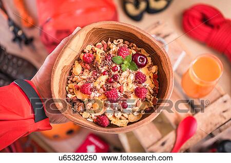 Stock Image - Overhead view of man's hand holding bowl of muesli above prepared climbing equipment. Fotosearch
