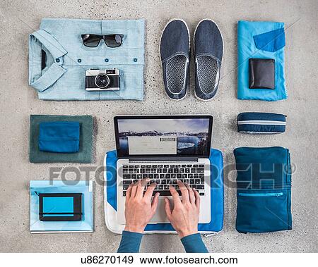 Overhead view of man's hands typing on laptop surrounded by travel packing items, with blue shirt, retro camera, wash bag and notebook View Large Photo Image Stock Photo - Overhead view of man's hands typing on laptop surrounded by travel packing items, with blue shirt, retro camera, wash bag and notebook. Fotosearch