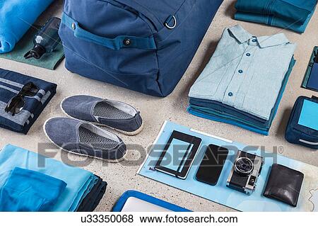 Stock Photo - Overhead view of travel packing with blue shirt, retro camera, training shoes, smartphone and notebook. Fotosearch