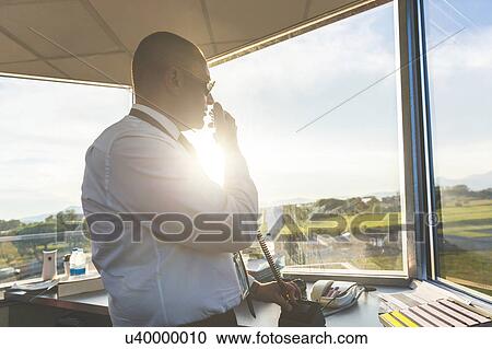 Stock Image - Pilot in control tower of small airport, using telecommunications system. Fotosearch