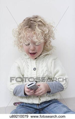Stock Photo - Portrait of blond girl (4-5) playing with mobile phone. Fotosearch