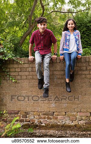 Stock Image - Portrait of brother and sister sitting on wall. Fotosearch